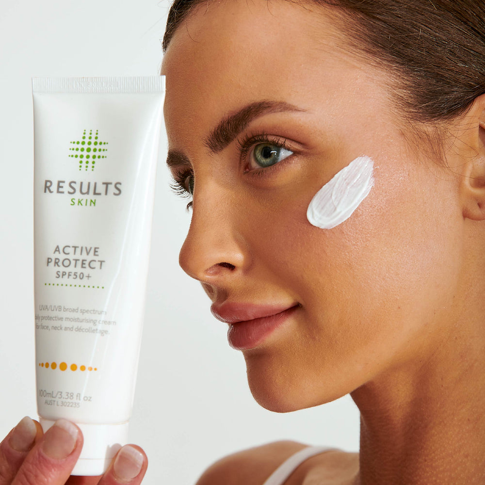 Woman holding Results Skin Active Protect SPF50+ with sunscreen applied to her cheek